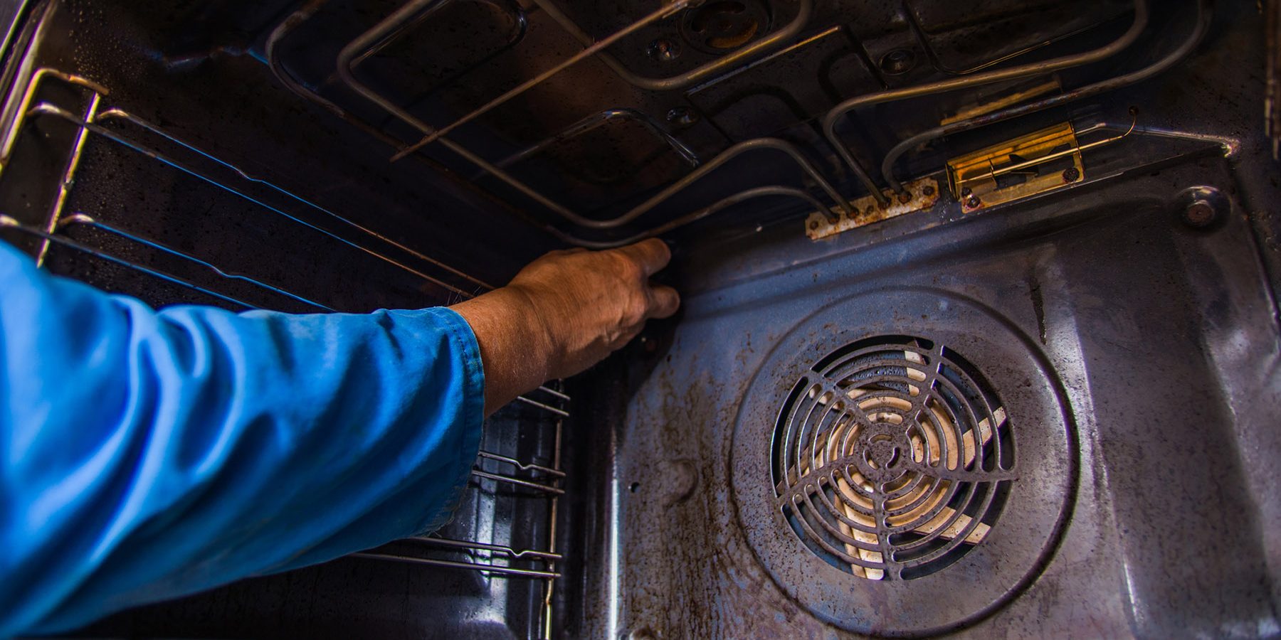 Repairman fixing the motor fan inside in the oven